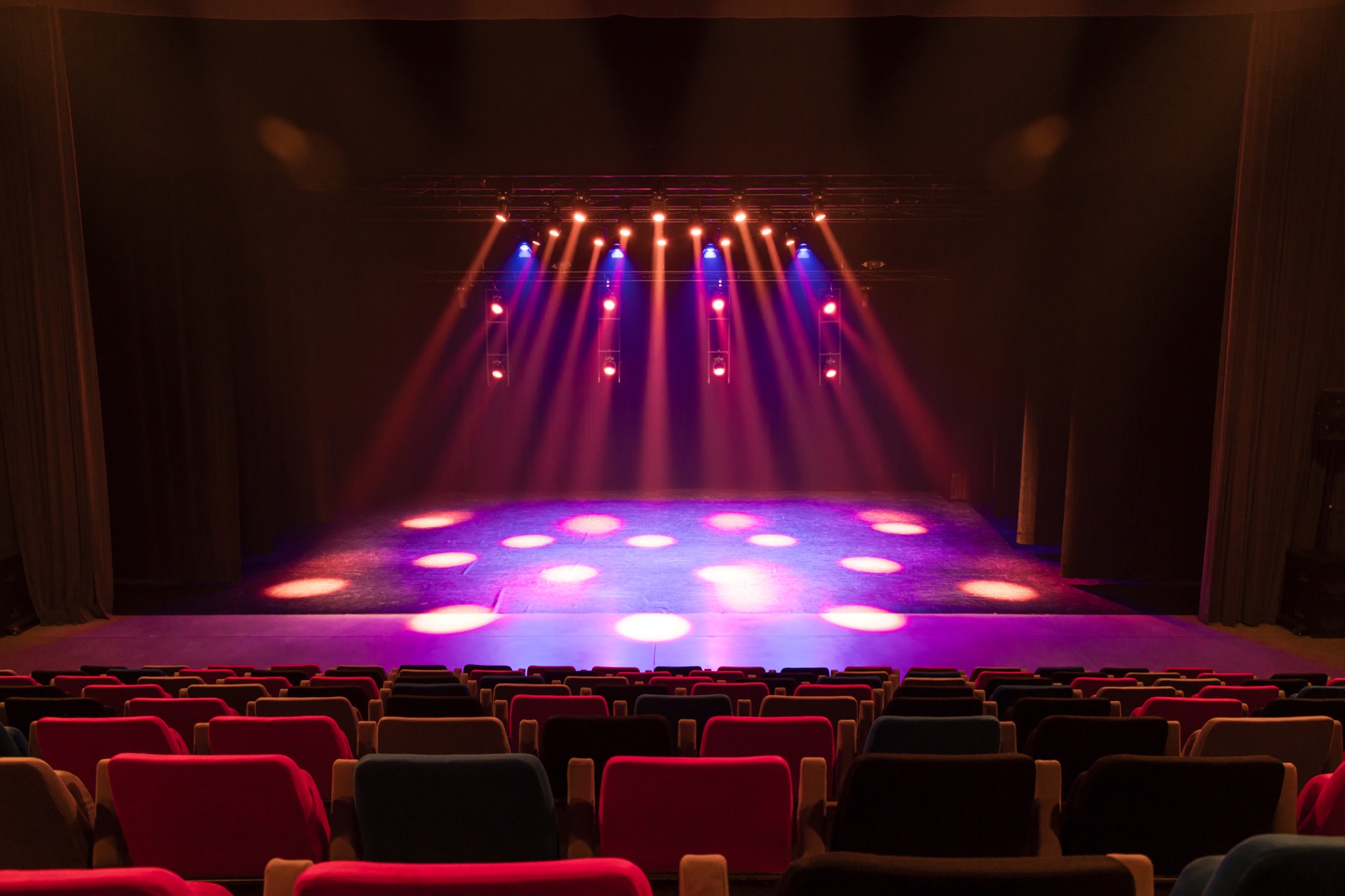 Auditorium van Meeting- en Eventcentrum Staf Versluys met verlicht podium en rode zitplaatsen